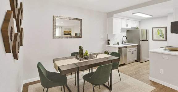 A modern dining room with a table set for two and a kitchen in the background.