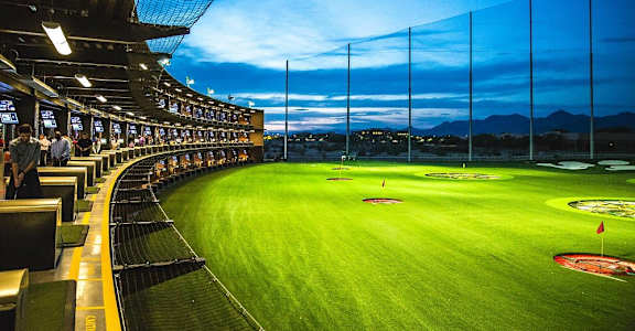 A cricket stadium is shown with a green field and a crowd of spectators.