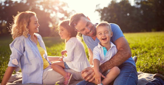 A family of four is sitting on a blanket in a field.