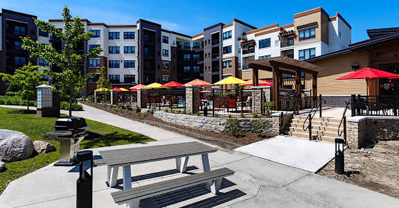 A park area with a bench and a fire hydrant in front of apartment buildings.
