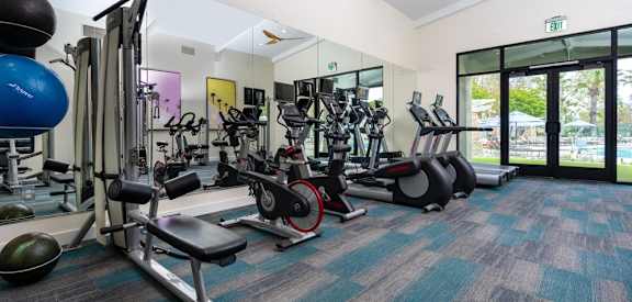 a gym with cardio equipment and weights in a building with windows