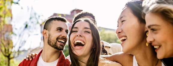 Three people are laughing together outdoors.