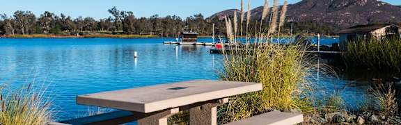 A picnic table sits in front of a lake with a mountain in the background.