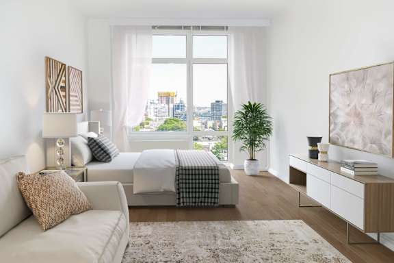 A modern bedroom with a large window overlooking the city at The Maximilian Apartments, Long Island City