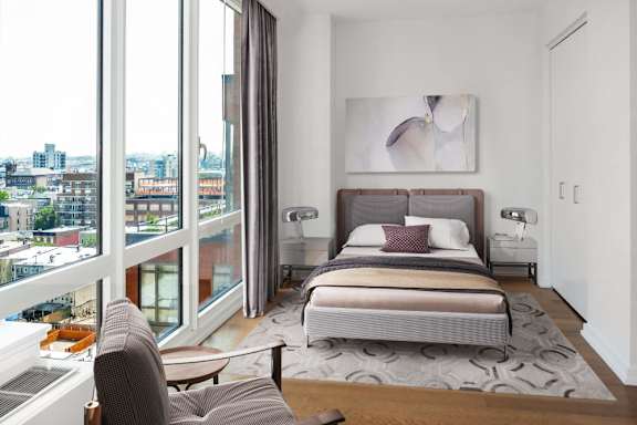 A bedroom with a large bed and a view of the city at The Maximilian Apartments, Long Island City, New York