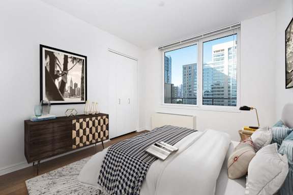 A bedroom with a large bed and a city view through the window at The Maximilian Apartments, Long Island City, NY, 11101