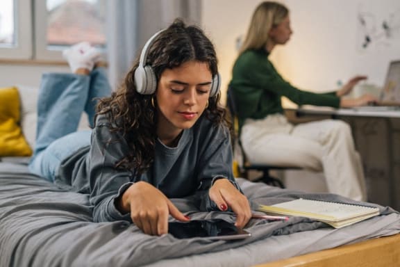 a young woman laying on a bed listening to headphones and using a laptop