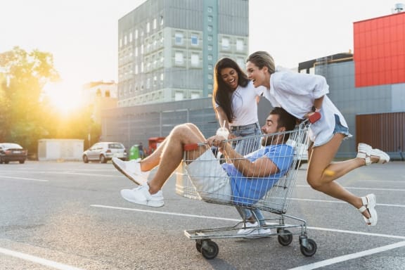 a man is lying in a shopping cart with two women