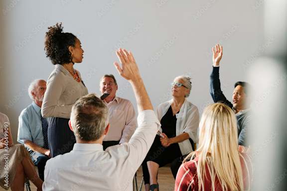 A group of people are gathered in a circle, with one person raising their hand.