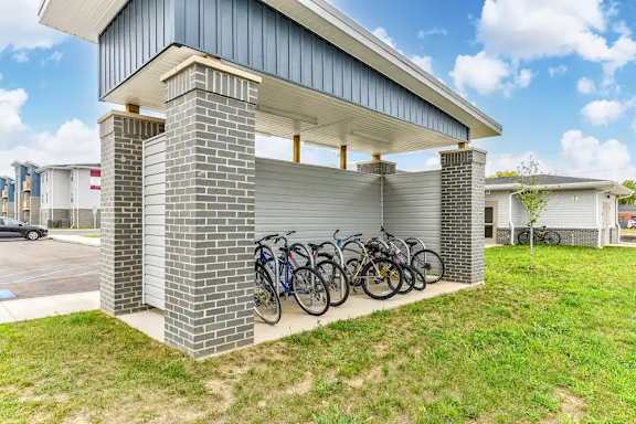 A row of bicycles are parked in a bike rack under a covered area.