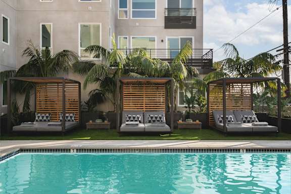A pool with a wooden sunshade and a building in the background.