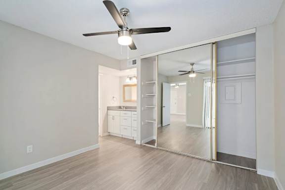 A spacious room with a ceiling fan and a mirrored closet door.