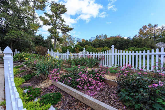 a garden with flowers in front of a white fence at The Residences at the Manor Apartments, Frederick, 21702