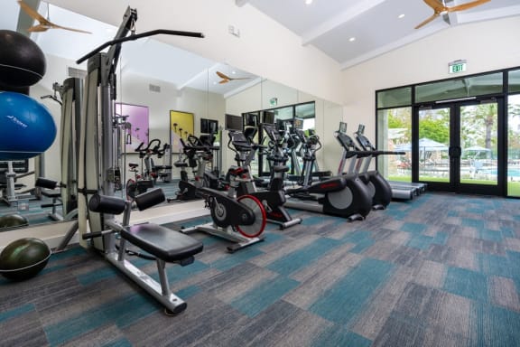 a gym with cardio equipment and weights in a building with windows