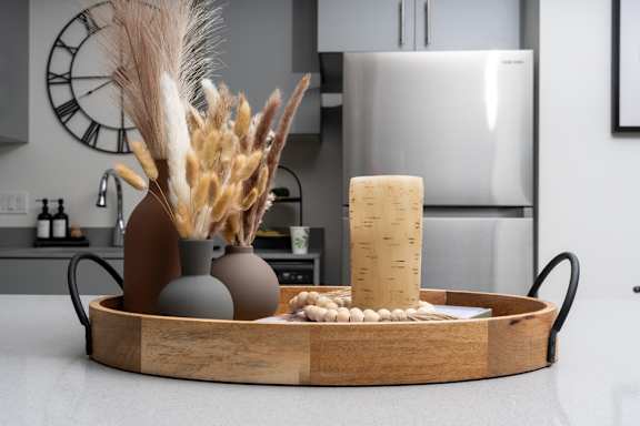 A wooden tray with a vase, a candle, and some decorative items on a kitchen counter.