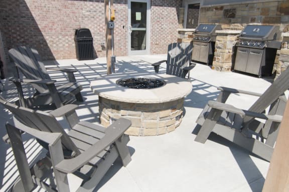 Outdoor chairs positioned around a firepit with grills off to the side
