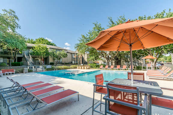 Pool deck with orange umbrella and lounge seating at The Colony Apartments, Universal City, TX 78148