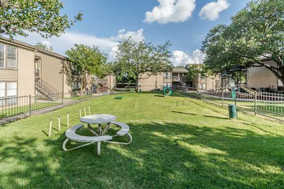 Fenced dog park with play equipment and picnic table at The Colony Apartments, Universal City, TX