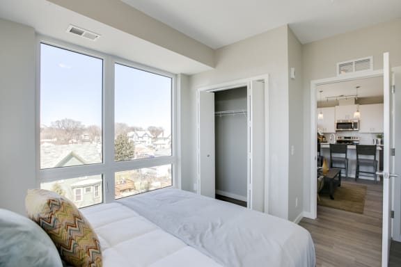 Bedroom with tall window and open closet looking out into the living and dining area