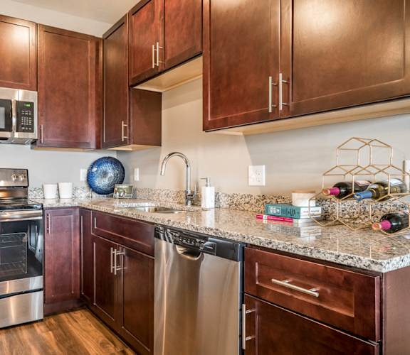 Kitchen featuring light granite countertops, dark cabinetry and stainless-steel appliances at 360 at Jordan West best new apartments West Des Moines IA 50266