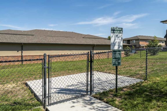 a sign on a chain link fence surrounded grassy dog park