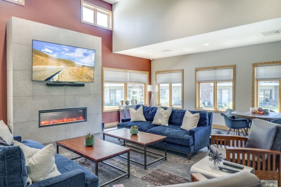 Spacious clubhouse with comfortable couches and chairs, tables, large TV, cozy fireplace, and lots of natural light coming in from the windows at Fountain Glen Apartments in Lincoln NE