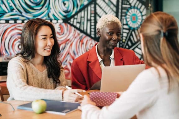 a group of women sitting at a table with a laptop