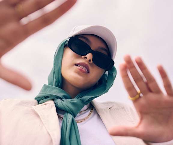 a woman wearing sunglasses and a hijab and holding her hands up