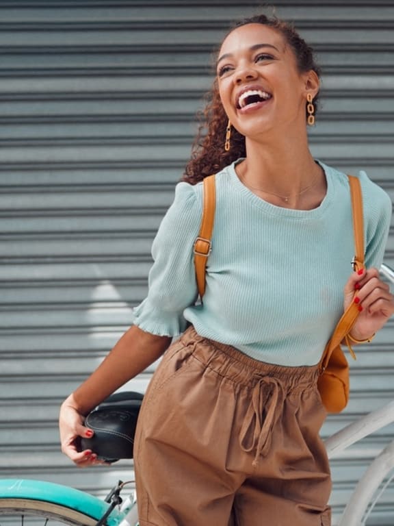 a woman laughing while walking her bike down the street