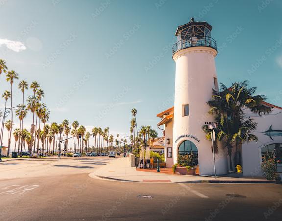 A white lighthouse with a black top stands in front of a building with a sign that reads "SANTA BARBARA".