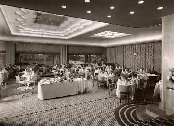 A black and white photo of a banquet hall with tables set up for an event.