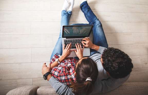 two people sitting on a couch with a laptop