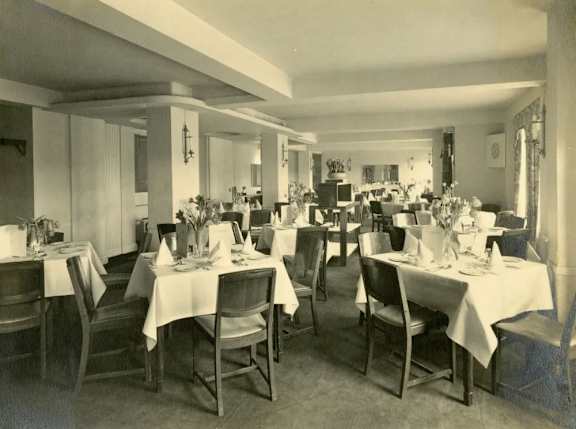 A black and white photo of a restaurant with tables set for dining.