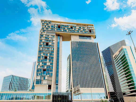 A tall building with a unique design stands out among other modern buildings.
