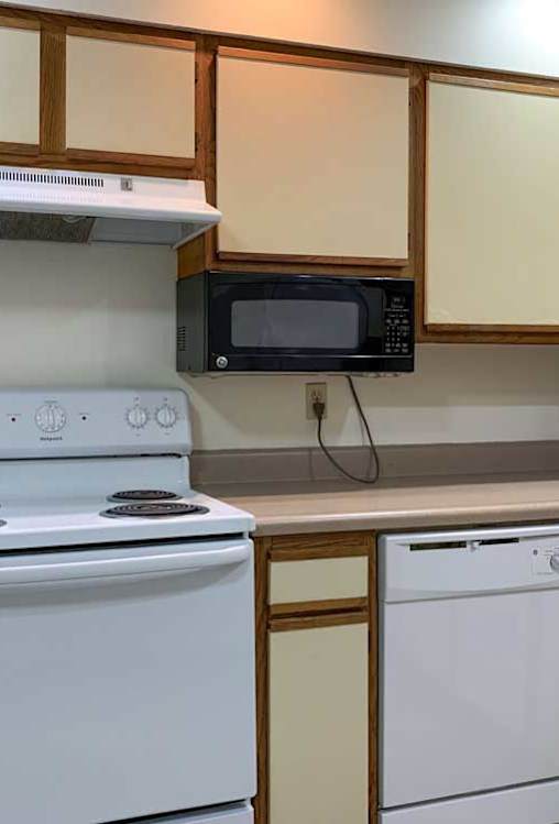 a kitchen with a white stove and dishwasher, a mounted microwave, and white and wooden cabinets