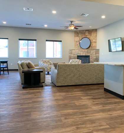a tv lounge with a stone fire place and a grey couch, with hardwood flooring