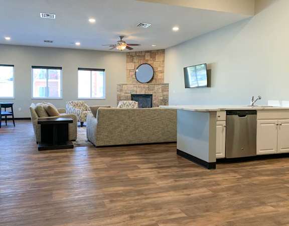 a tv lounge with a stone fire place and a grey couch, with hardwood flooring