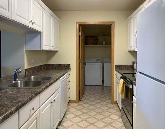 a kitchen with white cabinets, dark counter tops, vinyl flooring, and a white fridge