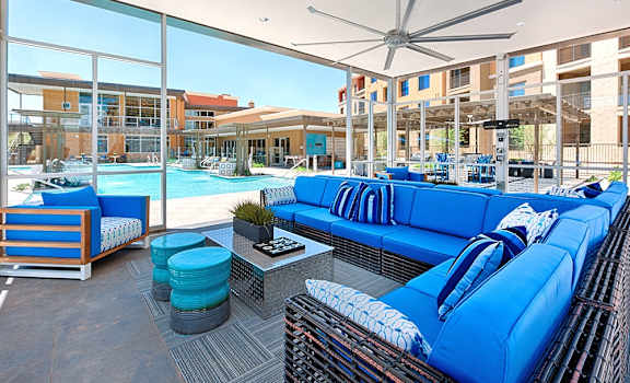 a patio with blue couches and chairs and a pool in the background at 56 North, Phoenix, 85054