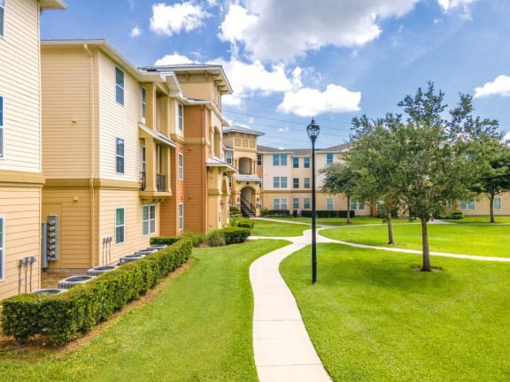 a sidewalk leading to an apartment building with grass and trees