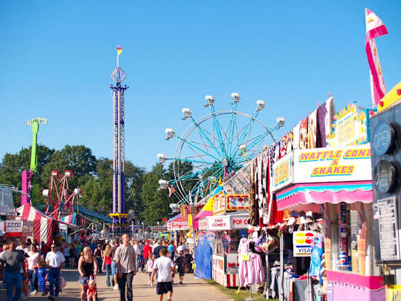 A fair with a Ferris wheel and a waffle coney stand.