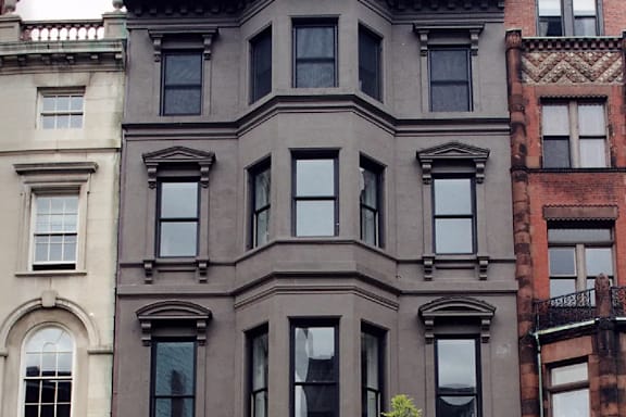 A brown building with many windows sits next to a green tree.