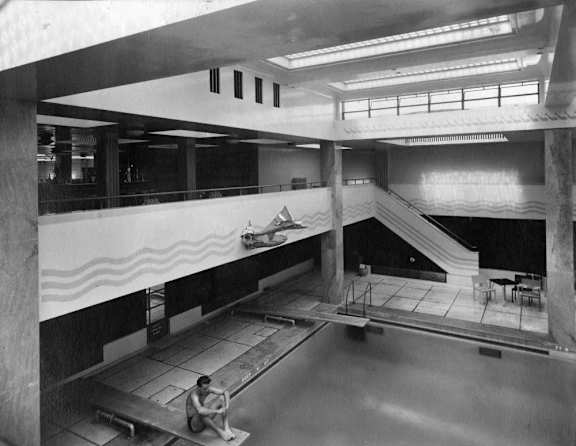 A black and white photo of a man sitting on a bench in a large indoor space.