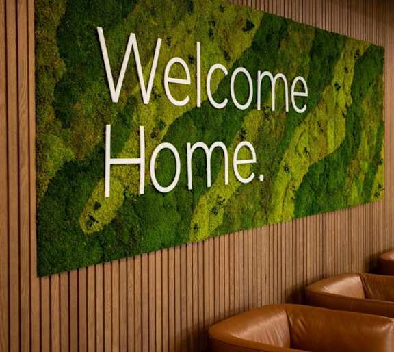 a sign that reads welcome home on a wall of moss