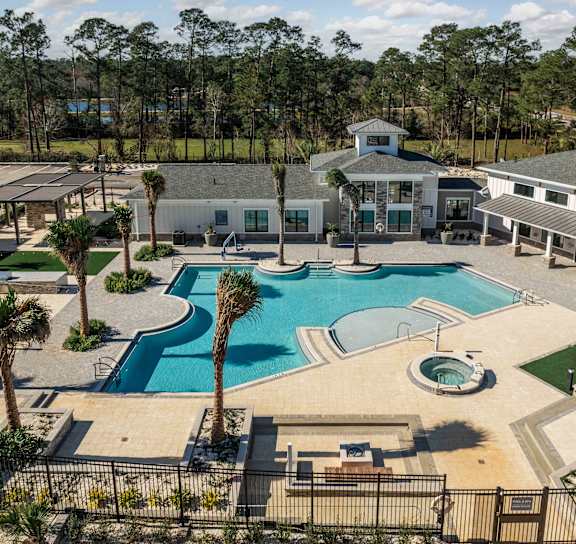 A large swimming pool surrounded by palm trees and a building in the background.  at The Quinn Luxury Apartments, Pensacola, FL