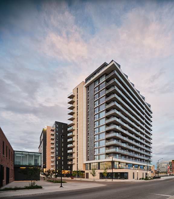 A modern multi-story building with a curved facade and balconies is situated on a street corner.