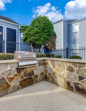 a patio with a stone wall and a grill in front of a house