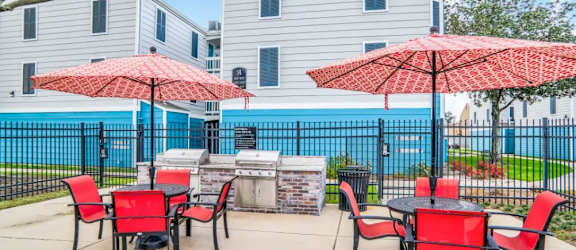 a patio with a grill and tables with red chairs and umbrellas