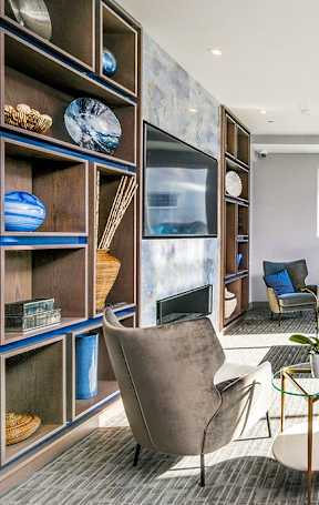 A modern living room with a grey sofa, a blue ottoman, and a glass coffee table.