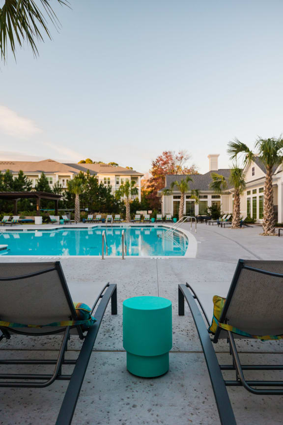 a pair of lounge chairs sit in front of a swimming pool with palm trees in the background